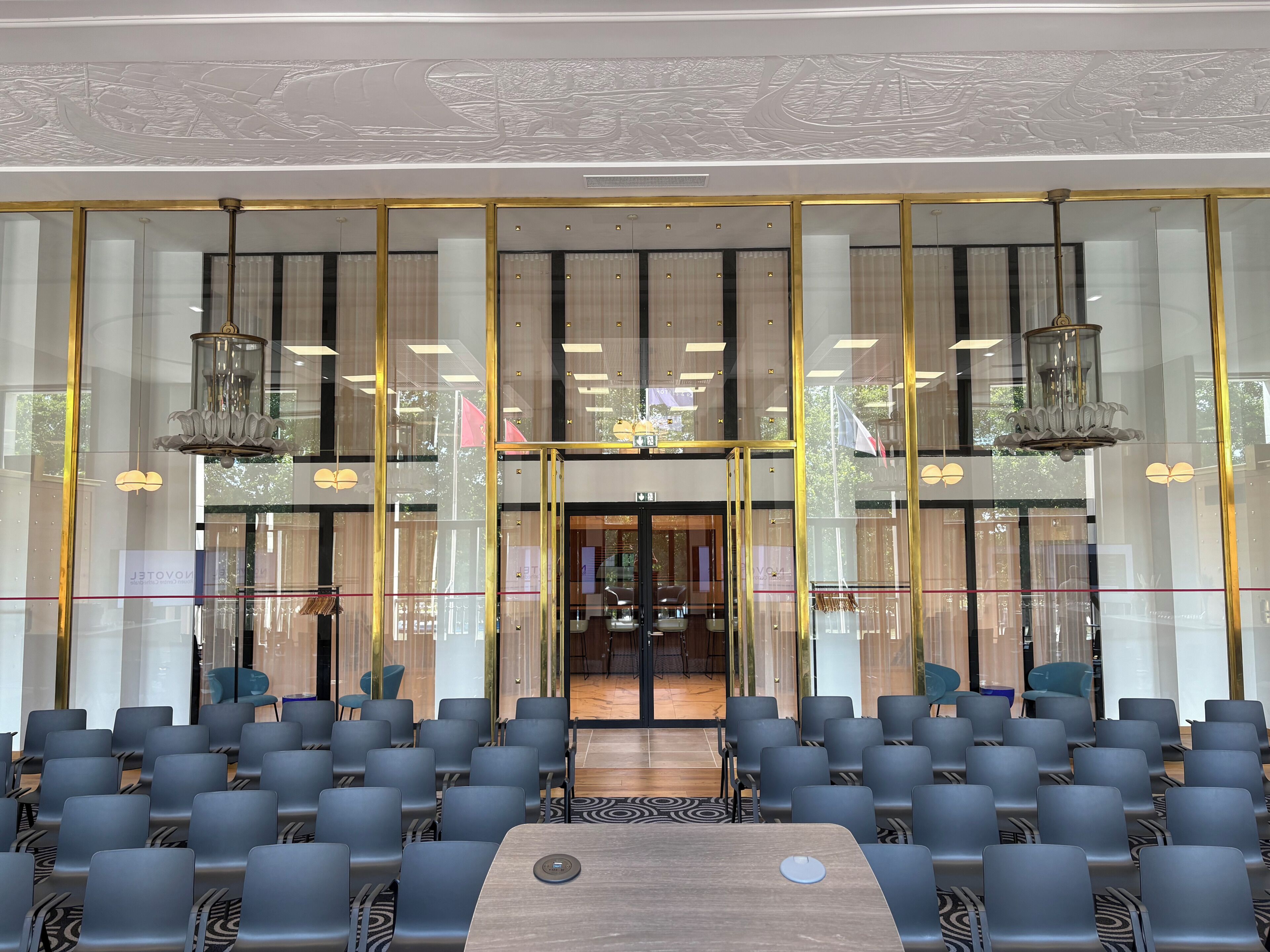 Un hall d’hôtel avec des rangées de fauteuils, un comptoir d’accueil et une grande fenêtre donnant sur la rue.