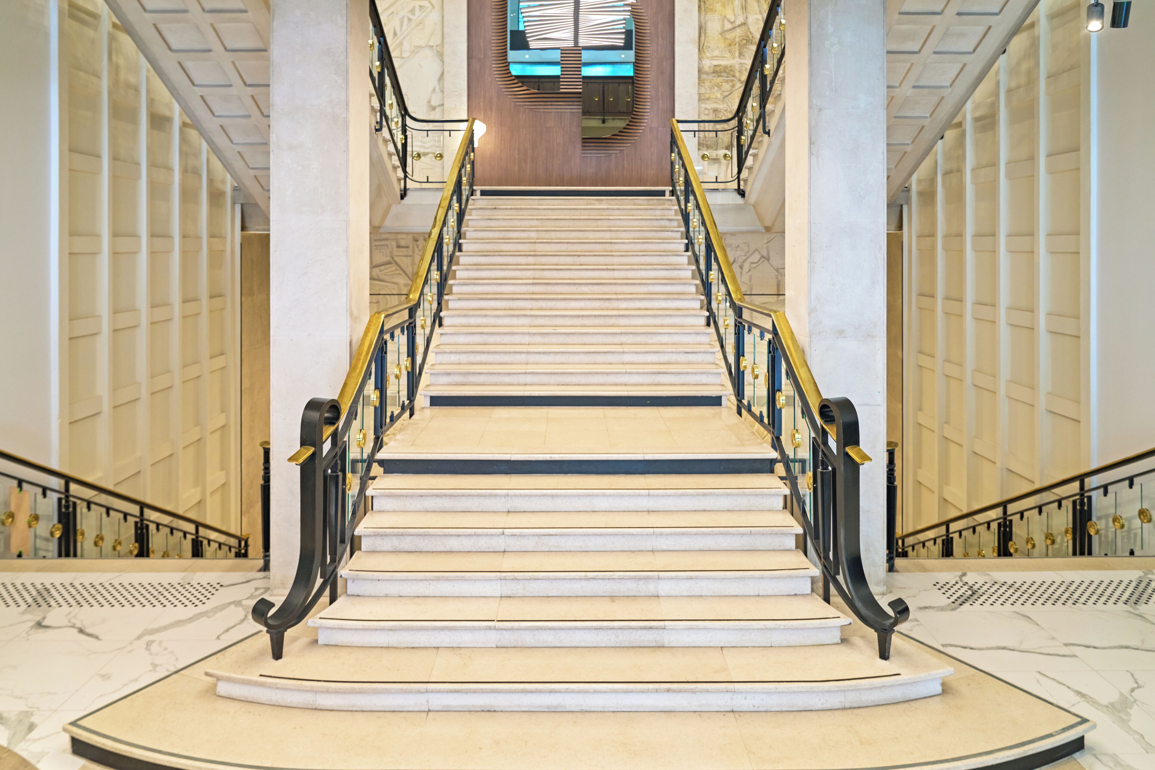 A grand staircase with marble steps and black railings, leading to a wooden panel wall with a large window.