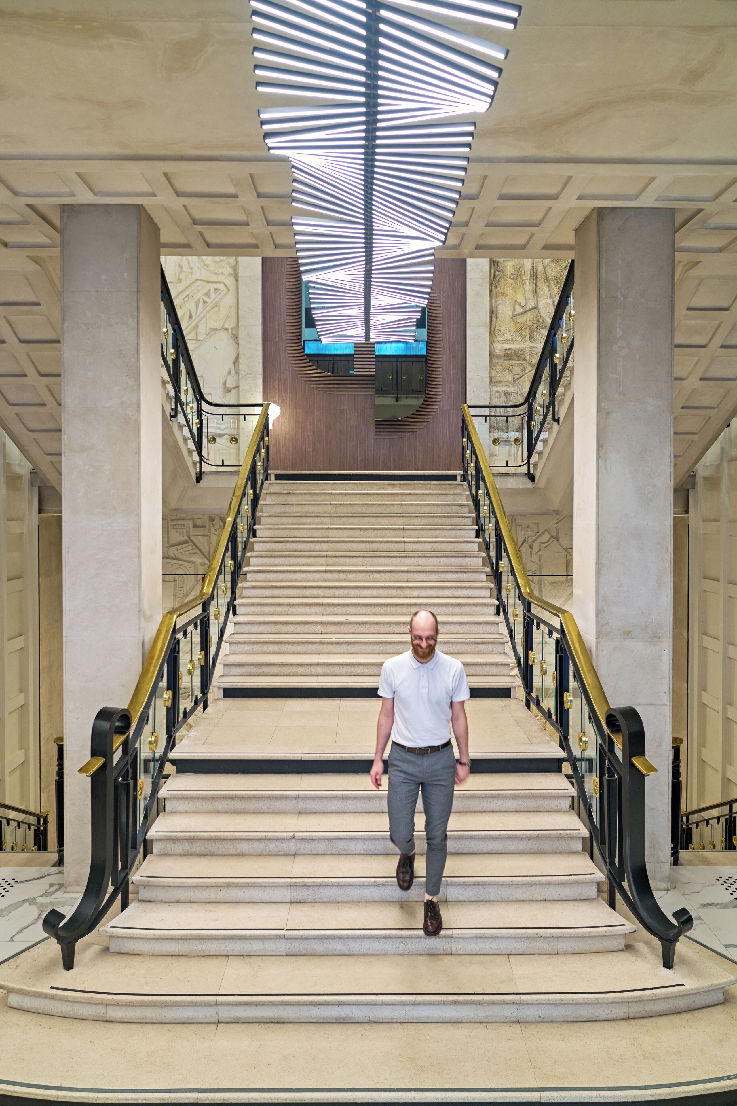 Ein Mann geht eine imposante Treppe mit modernem Deckenstil und Marmorstufen hinunter.
