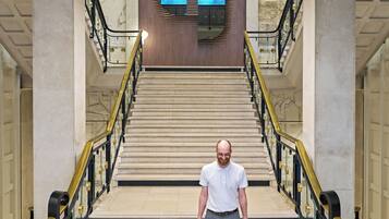 Ein Mann geht eine imposante Treppe mit modernem Deckenstil und Marmorstufen hinunter.