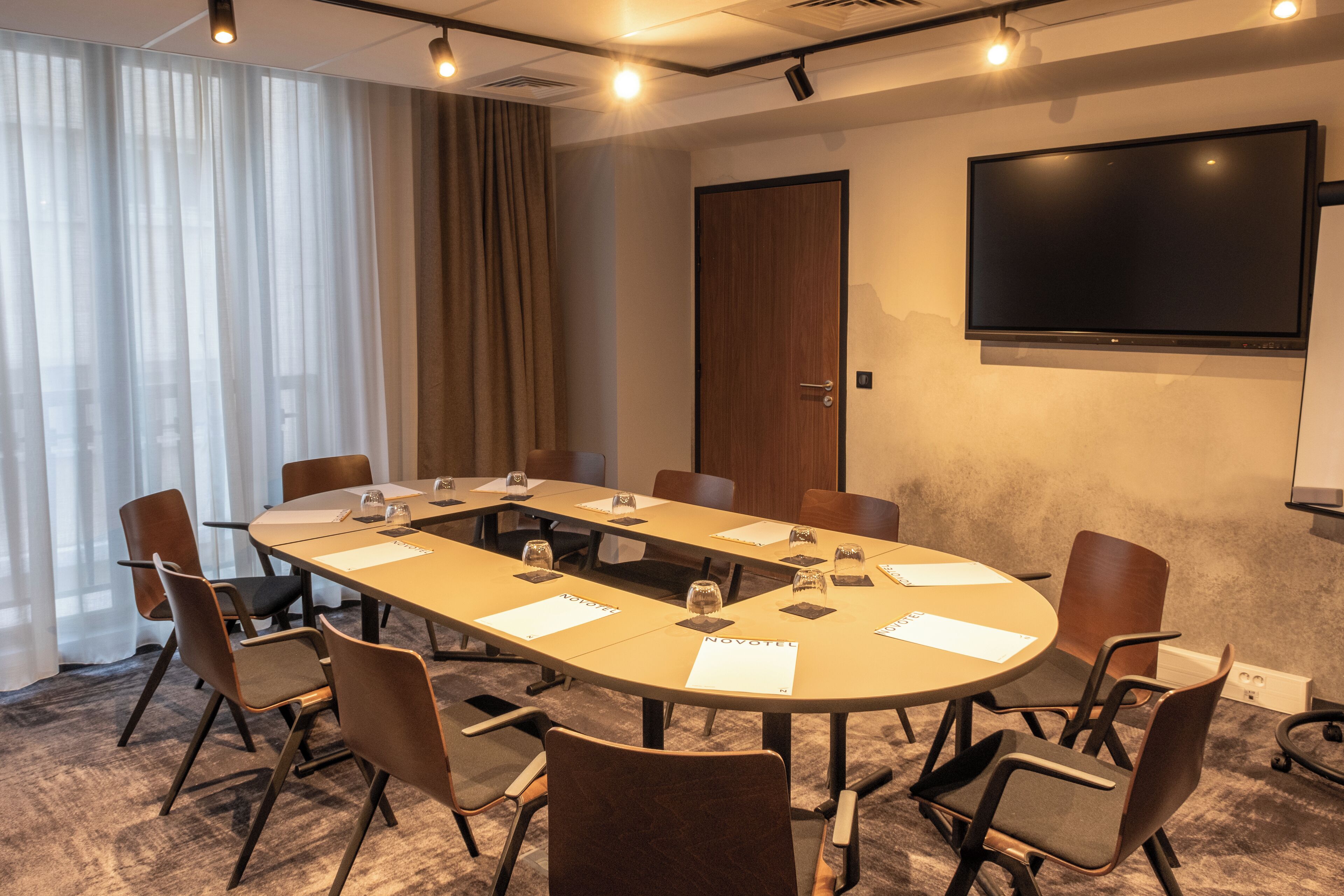 Une salle de conférence avec une longue table, des chaises, un téléviseur et une porte.