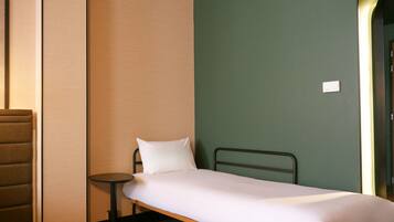A single bed with a white mattress and pillow, a small round table, and a green wall.
