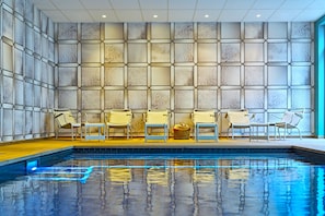 A swimming pool with a tiled floor, surrounded by lounge chairs and a wall with a geometric pattern. - Novotel Rouen Centre Cathédrale (Rouen)