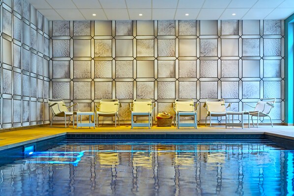 A swimming pool with a tiled floor, surrounded by lounge chairs and a wall with a geometric pattern. - Novotel Rouen Centre Cathédrale (Rouen)