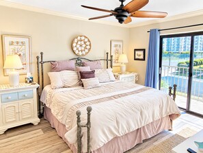A bedroom with a bed, bedside tables, a ceiling fan, and a view of the outside.