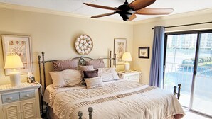 Une chambre à coucher avec un lit, des tables de chevet, un ventilateur de plafond et une vue par la fenêtre.