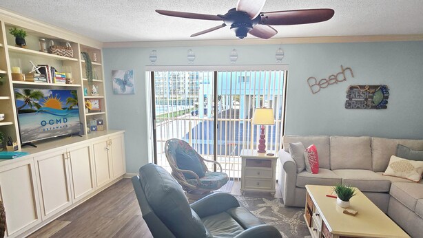 Un salon avec un téléviseur, un canapé, un fauteuil, une petite table et un ventilateur de plafond.