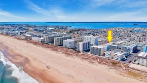 Vue aérienne d’une ville côtière avec de hauts immeubles, une plage et un ciel bleu dégagé.