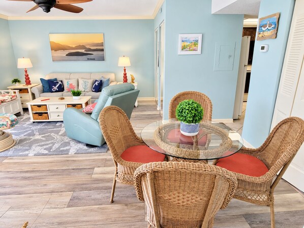 A living room with a sofa, chairs, a coffee table, and a dining area with wicker chairs and a glass table.