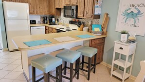 Une cuisine avec des meubles de rangement en bois, un îlot central doté de tabourets, un réfrigérateur et un four à micro-ondes.