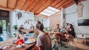 A spacious indoor area with wooden ceiling beams, round tables, and chairs. There are plants and a TV mounted on the wall. - Cama En Habitación Compartida Mixta En El Sector De La Candelaria - Medellín (Medellín)