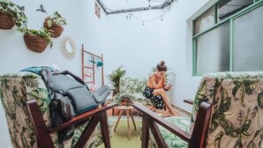 A cozy room with two chairs, a small table, and a window with green frames. - Cama En Habitación Compartida Mixta En El Sector De La Candelaria - Medellín (Medellín)