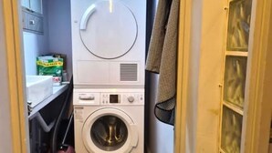 Ein kleiner Hauswirtschaftsraum mit einer Waschmaschine mit Frontlader, gestapelten Handtüchern und einem Wäscheständer.