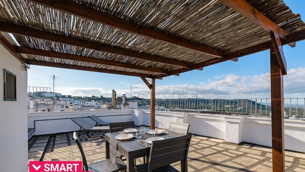 Eine Dachterrasse mit Esstisch, einer darüberliegenden Pergola und Stadtblick im Hintergrund.
