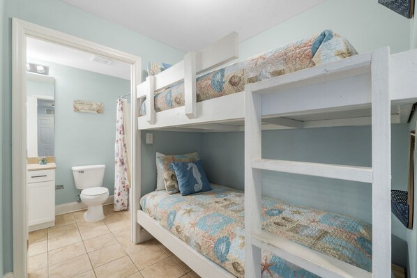 A bunk bed with a floral-patterned bedspread, a white sink, and a toilet in a bathroom with light blue walls.