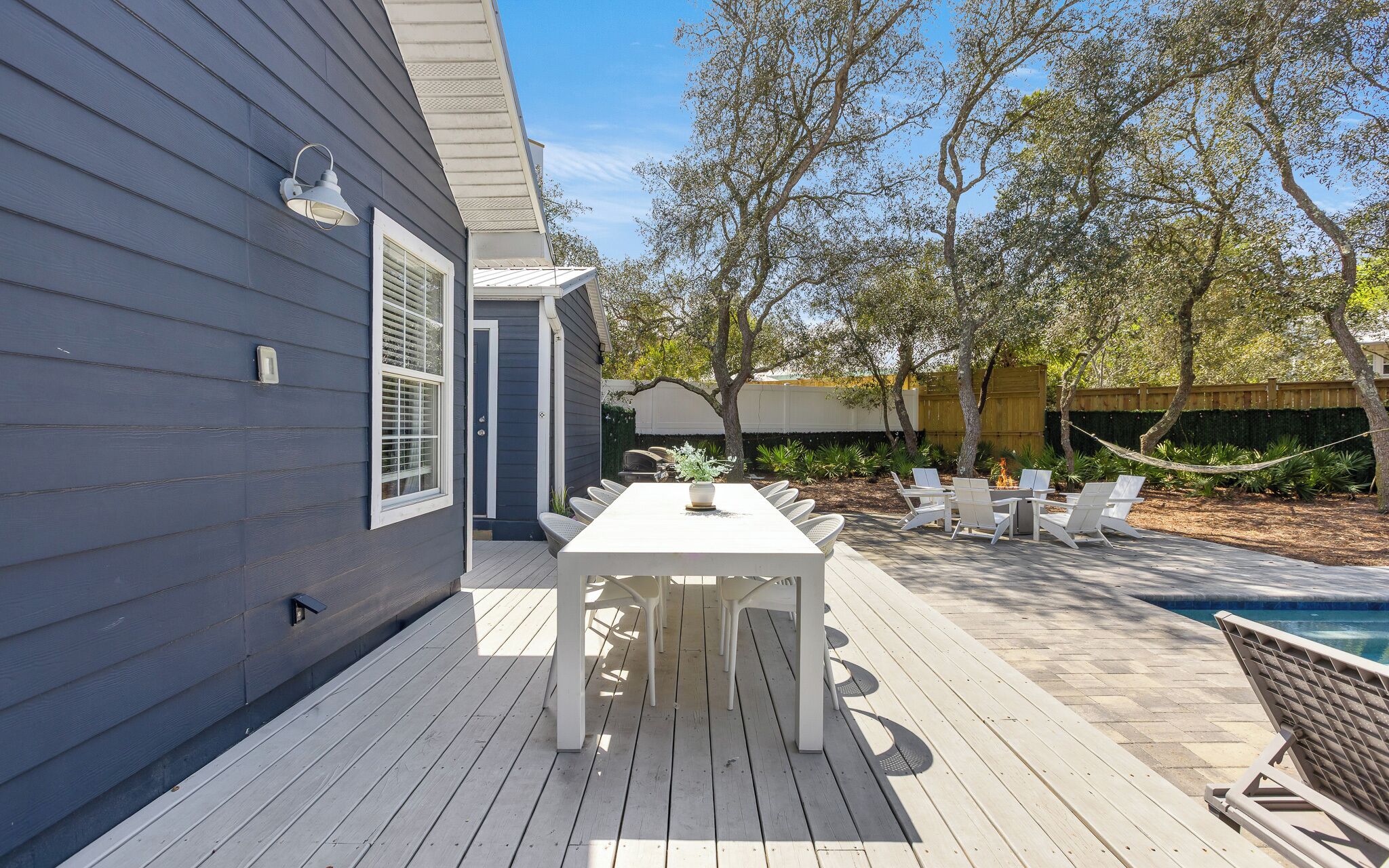 Une terrasse avec une table et des chaises blanches, une piscine et une clôture en bois.