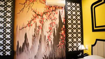 A hotel room with a bed, a nightstand with a lamp, and a wall with a floral mural.
