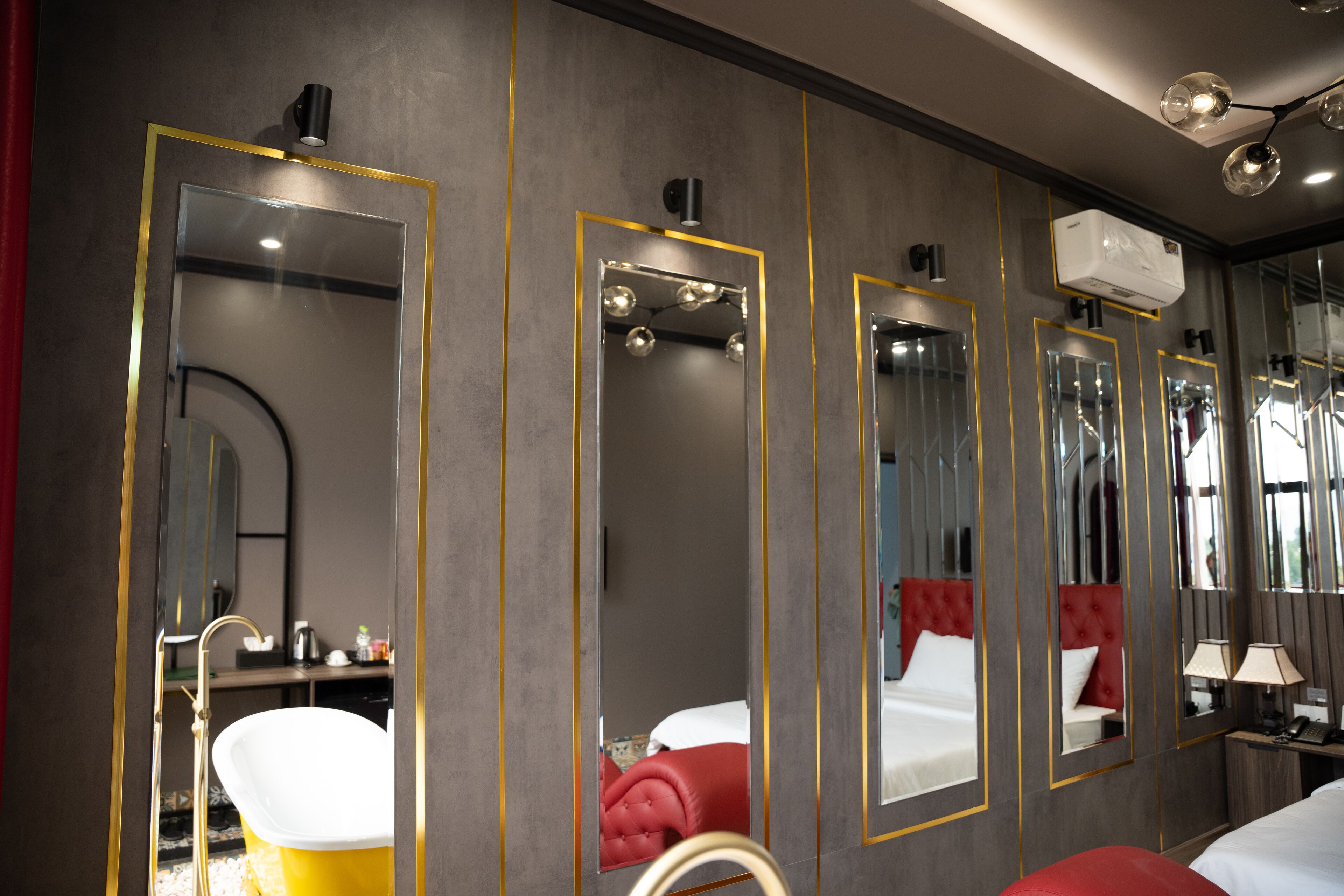 A hotel room with a large mirror, a vanity with a sink, a red chair, and a bed with white bedding.