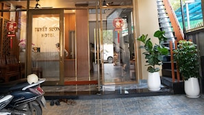 The entrance of Tuyet Soon Hotel with a tiled floor, a motorcycle parked outside, and potted plants near the entrance.