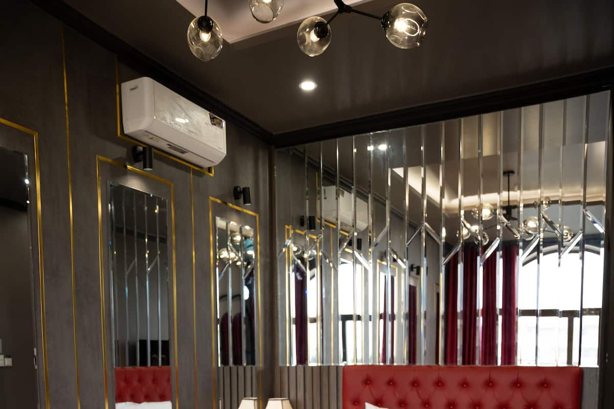 Une chambre d’hôtel moderne avec un grand lit, une tête de lit rouge rembourrée, un canapé rouge, un grand miroir et un sol à motifs.