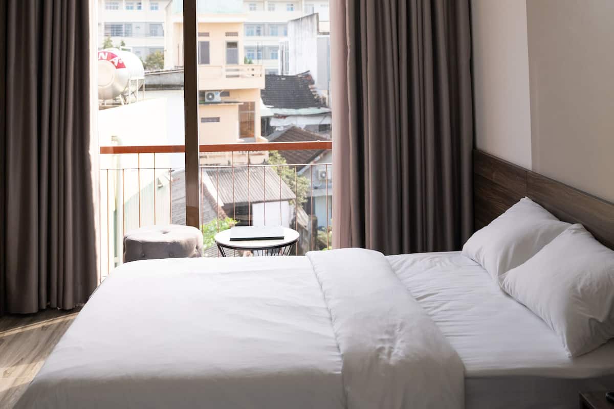 Une chambre d’hôtel avec un grand lit, une petite table ronde et un balcon avec des rideaux.
