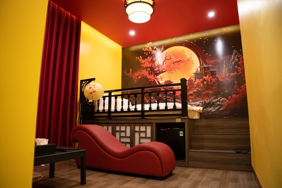 Une pièce avec un canapé rouge, une petite table, un lit avec une tête de lit en bois et une fresque murale représentant un cerisier en fleurs et un bâtiment traditionnel.