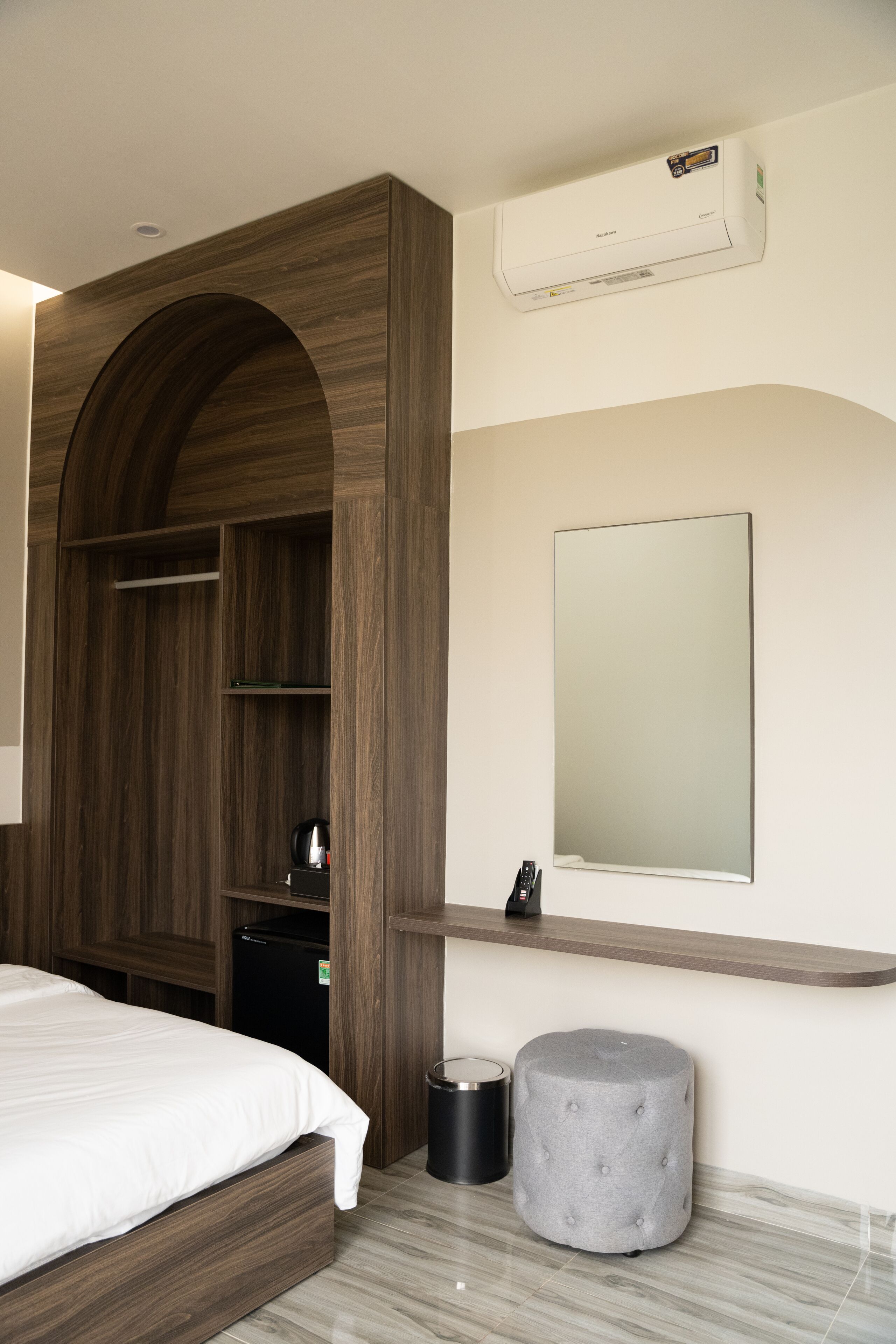 A bedroom with a bed, wardrobe, mirror, and a small ottoman.