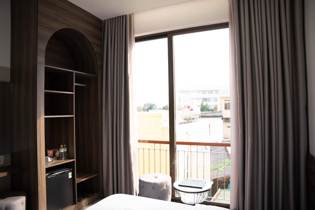 Une chambre d’hôtel dotée d’une grande fenêtre, d’un balcon, d’une armoire et d’une petite table avec une chaise.