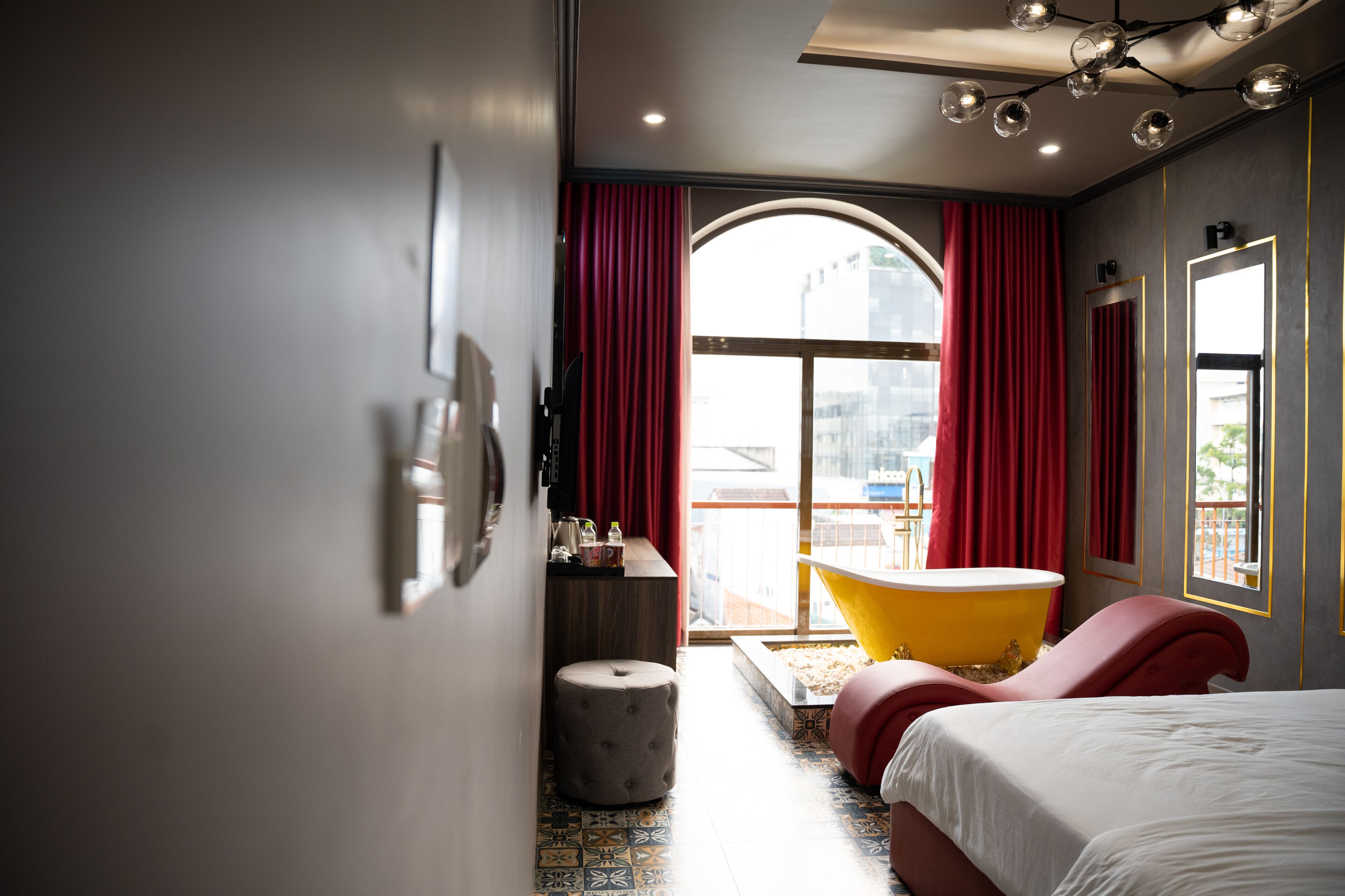 Et moderne hotelværelse med en stor seng, en rød sofa, et gult badekar og udsigt over byen gennem et stort vindue.