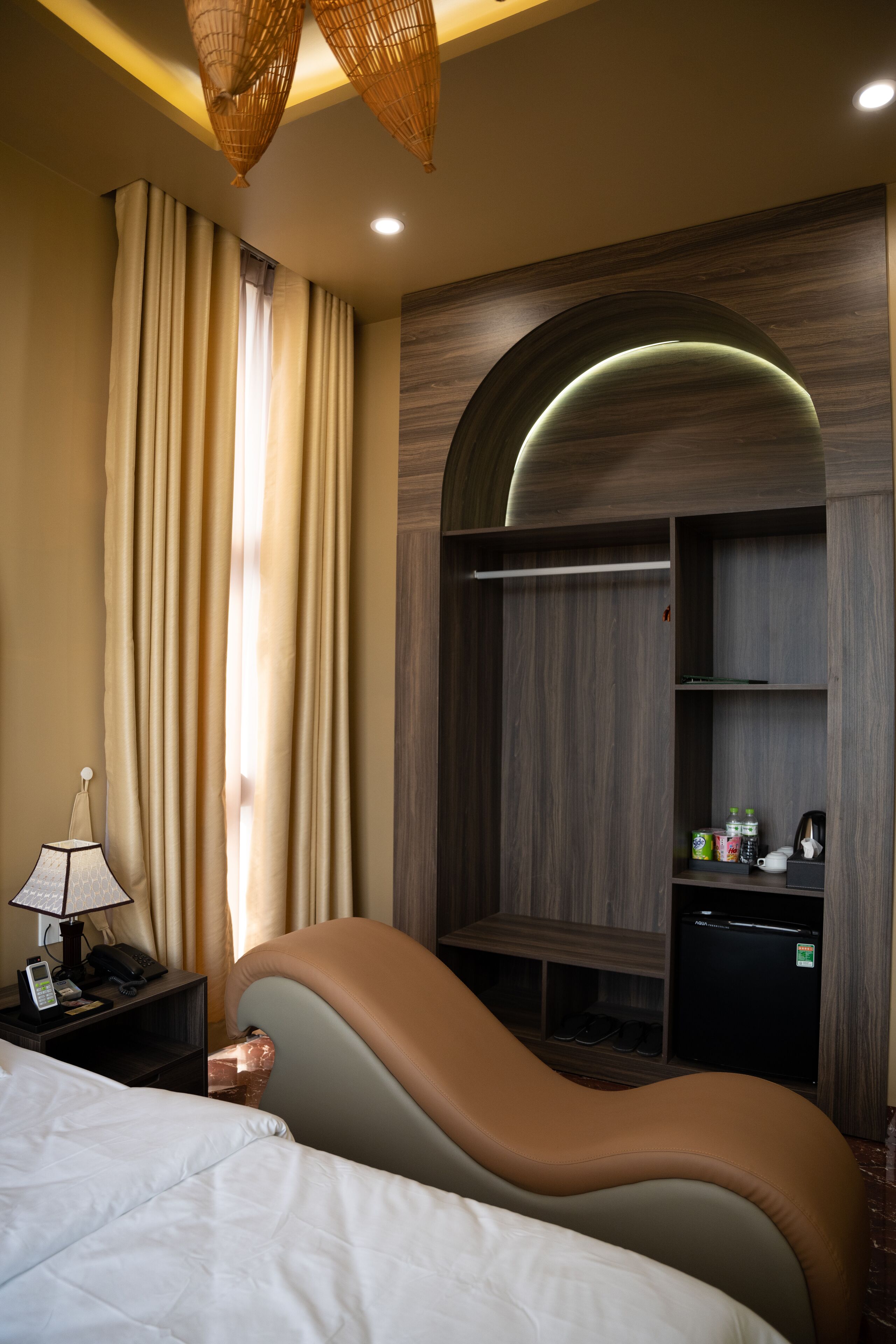 Une chambre d’hôtel comprenant un lit, une table de chevet avec une lampe, une armoire et un petit réfrigérateur.