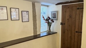 A reception area with a wooden counter, framed certificates on the wall, a window with blinds, and a wooden door. - Beautiful Cottage - 3 Bedrooms & 3 Bathrooms (Bakewell)