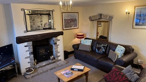 A cozy living room with a stone fireplace, a leather sofa, a wooden coffee table, and a television. - Beautiful Cottage - 3 Bedrooms & 3 Bathrooms (Bakewell)