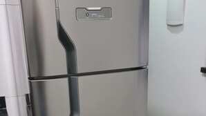 A stainless steel refrigerator with a handle, placed in a kitchen with white walls and a tiled floor.