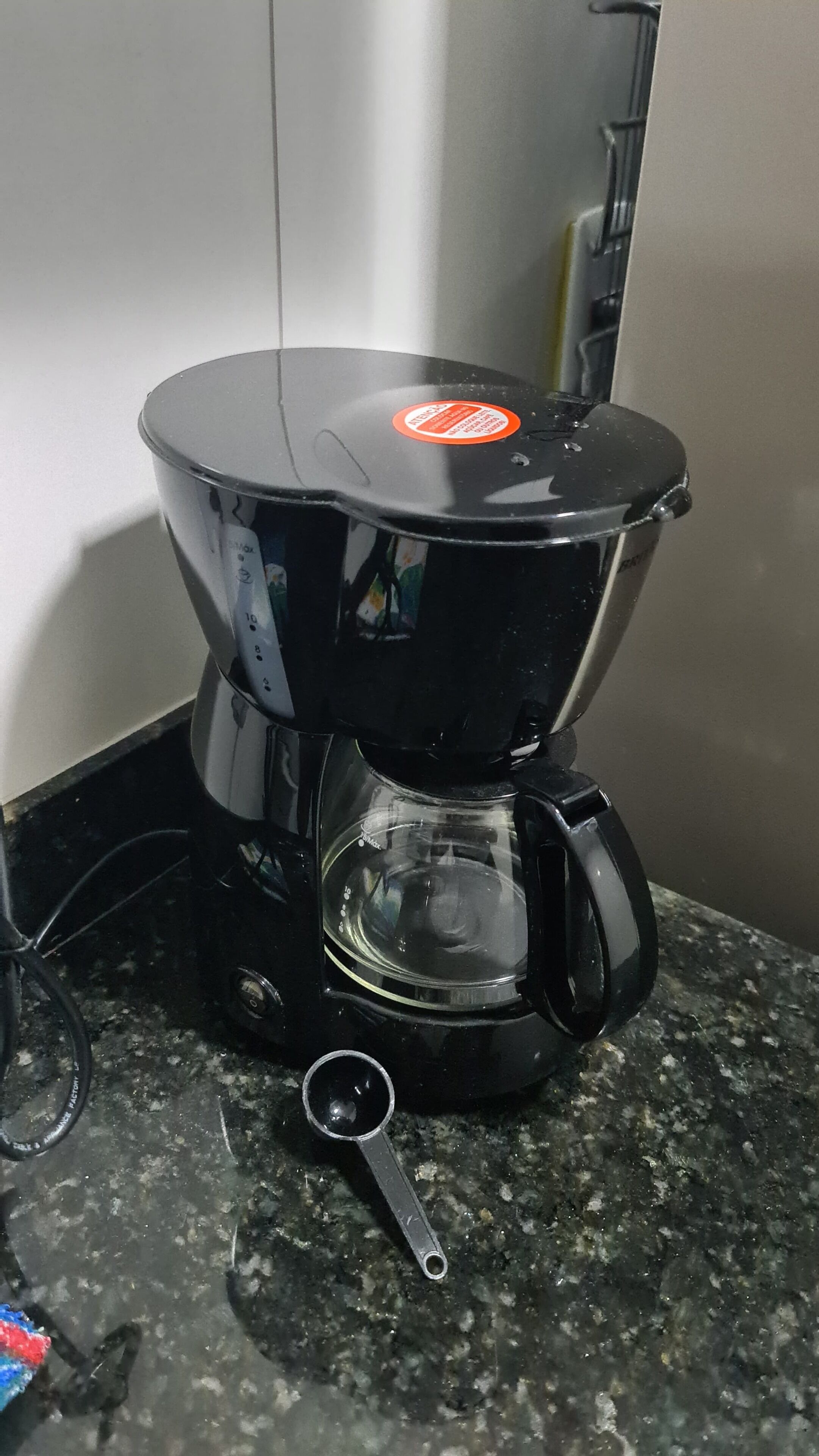 Une machine à café noire, dotée d’un réservoir d’eau transparent et d’un bac d’égouttage amovible, posée sur un comptoir en granit.
