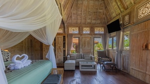 A room with a bed, sofa, and chairs, wooden walls, and a TV. - Billys Ayodya Villa (Perean Tengah)