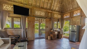 A spacious living area with wooden flooring, a flat-screen TV, a sofa, a coffee table, and a refrigerator. - Billys Ayodya Villa (Perean Tengah)