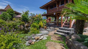 A traditional wooden house with a tiled roof, surrounded by lush greenery and a small pond.