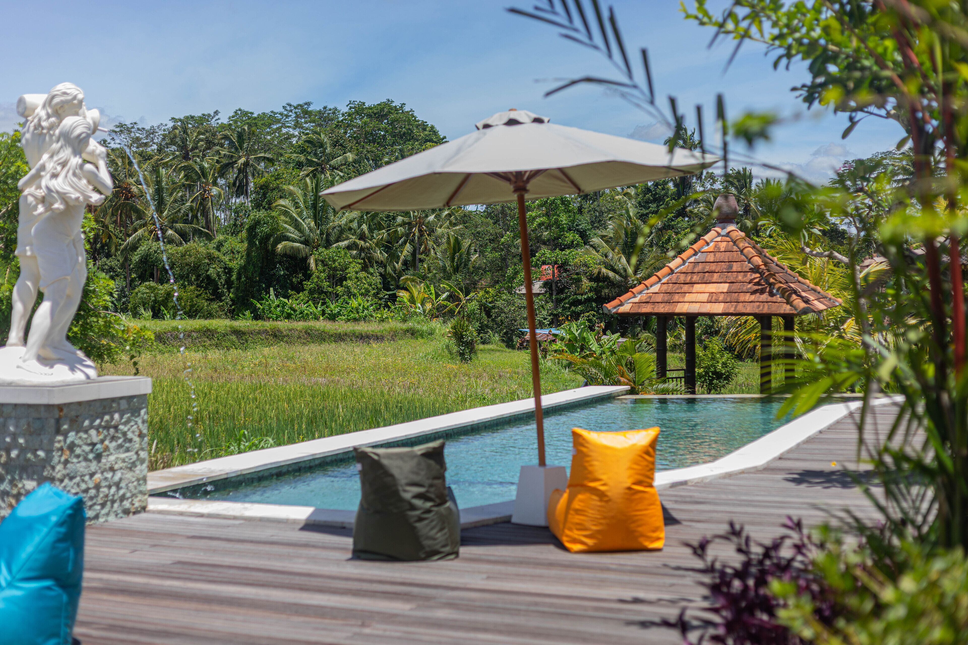 A poolside area with a statue, a gazebo, and a wooden deck with cushions.