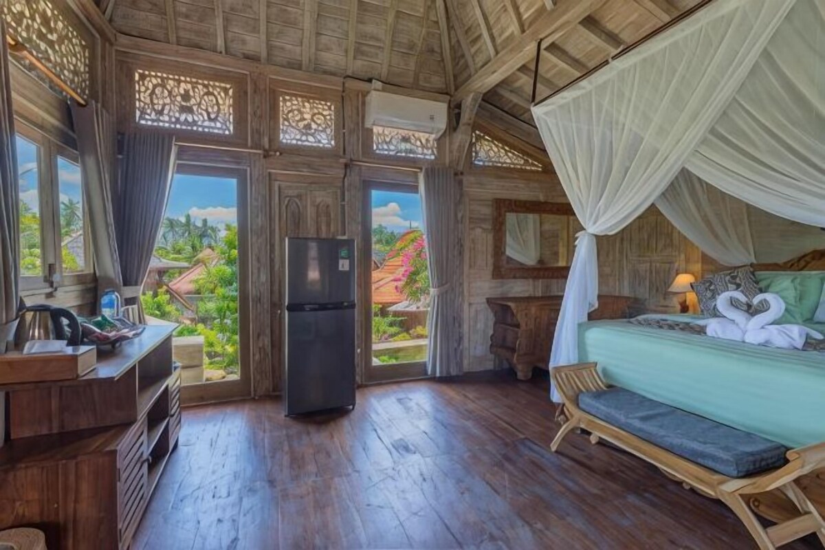 Quarto com uma cama, um banquinho, uma geladeira e vista para o exterior.