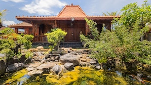 A traditional wooden building with a tiled roof, surrounded by a garden with rocks and plants, and a small pond. - Billys Ayodya Villa (Perean Tengah)