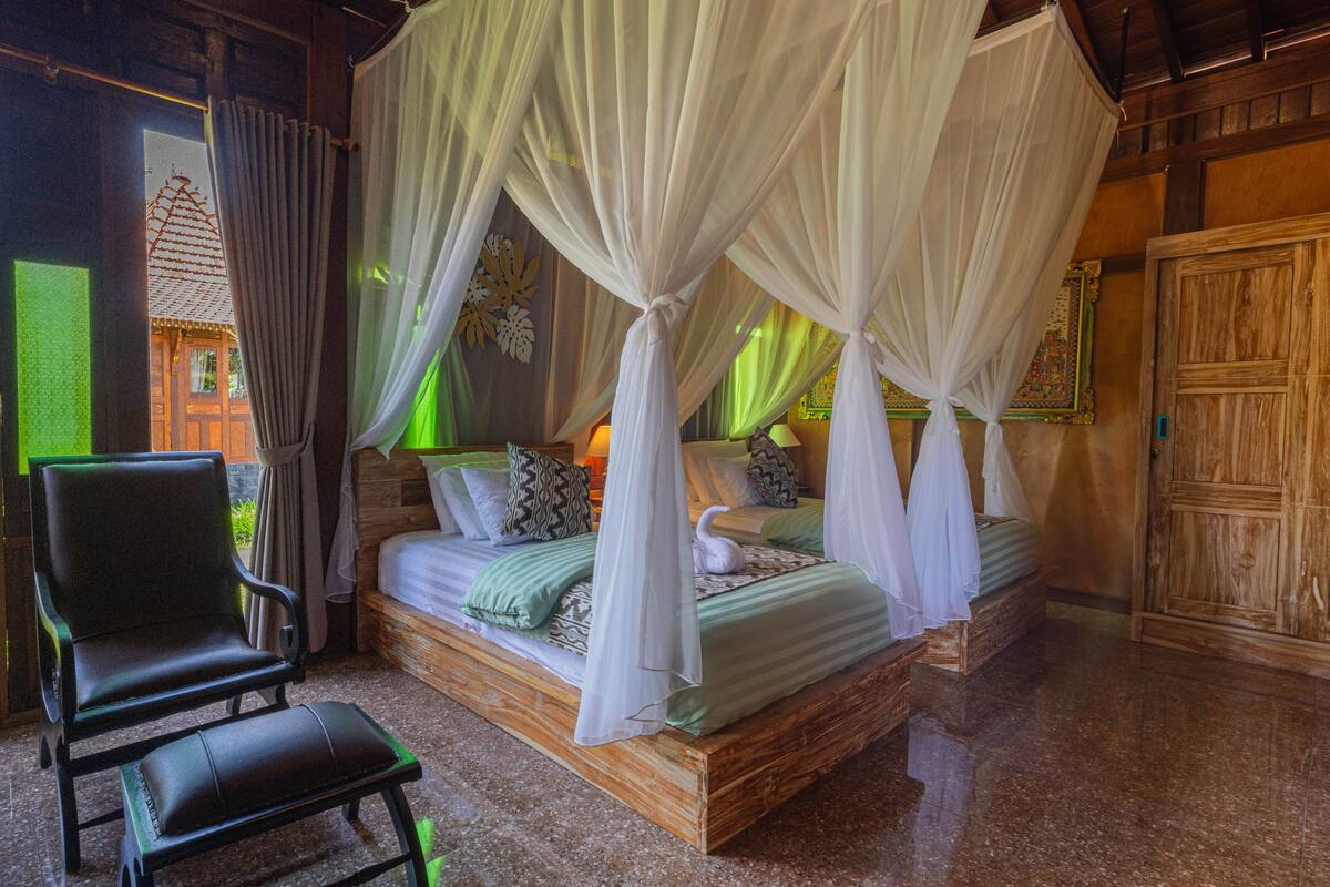 A bedroom with a four-poster bed, a chair, and a wooden wardrobe.