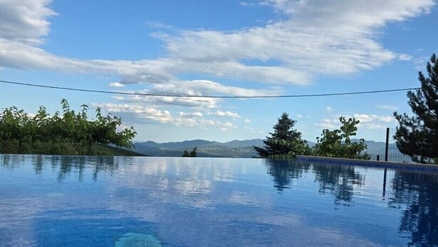 Un cielo azul despejado con nubes, una piscina con borde de azulejos y árboles al fondo.