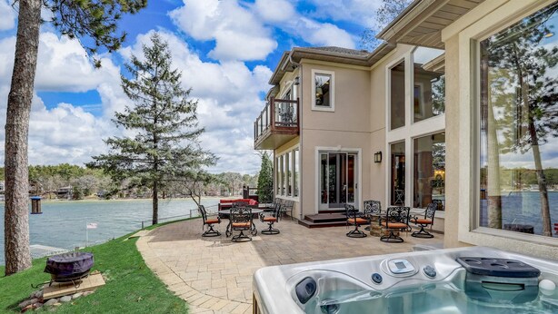 A two-story house with a patio area featuring outdoor furniture and a hot tub. - Luxury Lakefront! Hot Tub & Arcades! Sleep 24! (Wautoma)