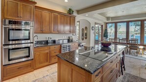 A modern kitchen with wooden cabinets, stainless steel appliances, and a large island. - Luxury Lakefront! Hot Tub & Arcades! Sleep 24! (Wautoma)