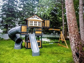 Une aire de jeux avec un toboggan, une balançoire et une cabane.