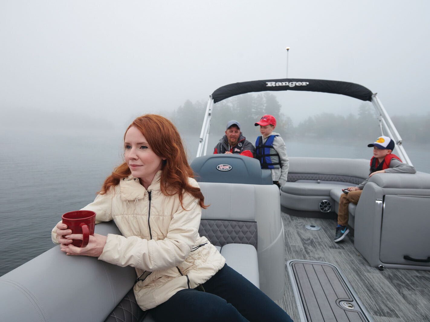 Un barco con un logotipo de "Ranger", una persona sosteniendo una taza roja y tres personas en la cubierta.