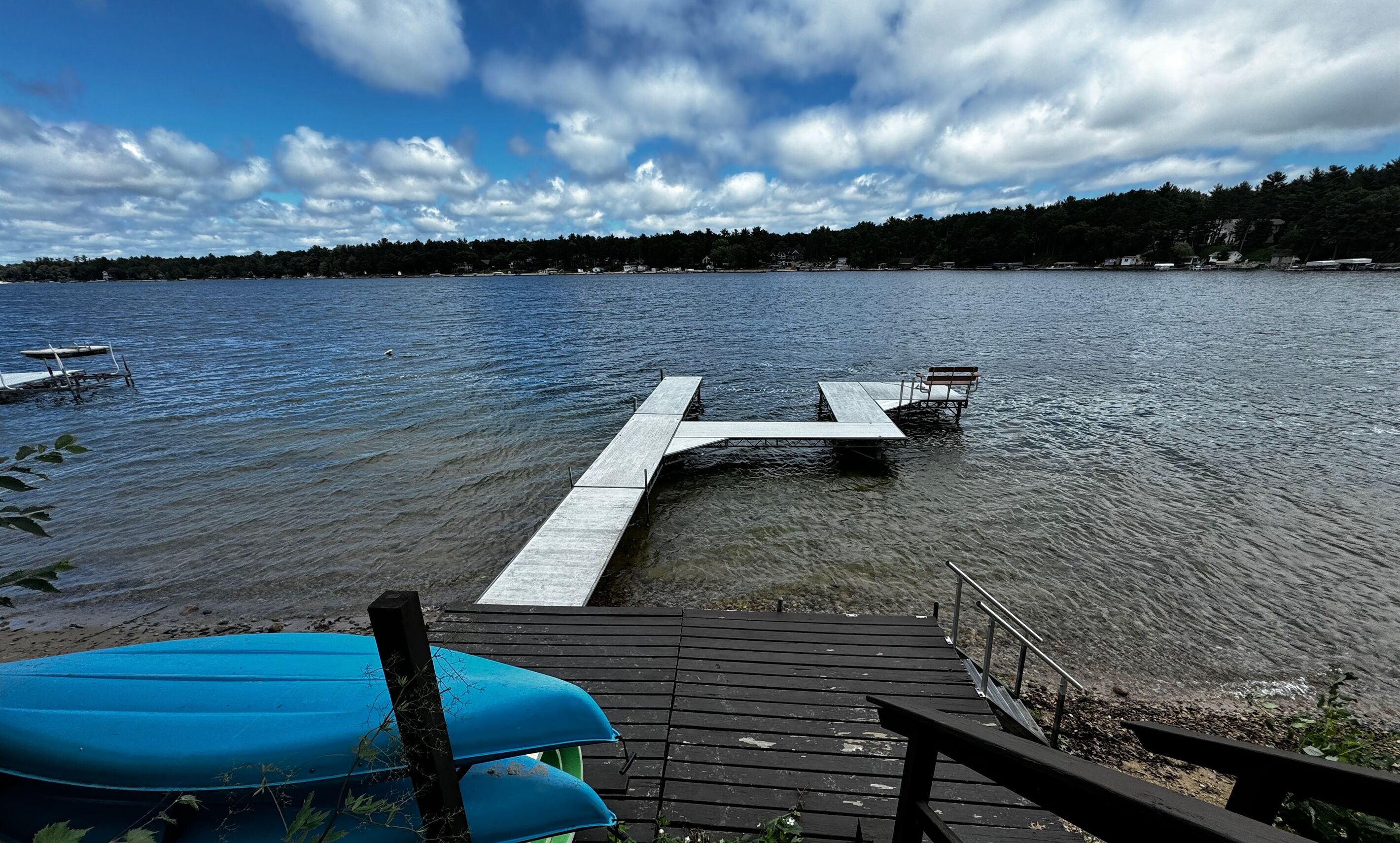 A wooden dock extending into a lake with a bench and a kayak.