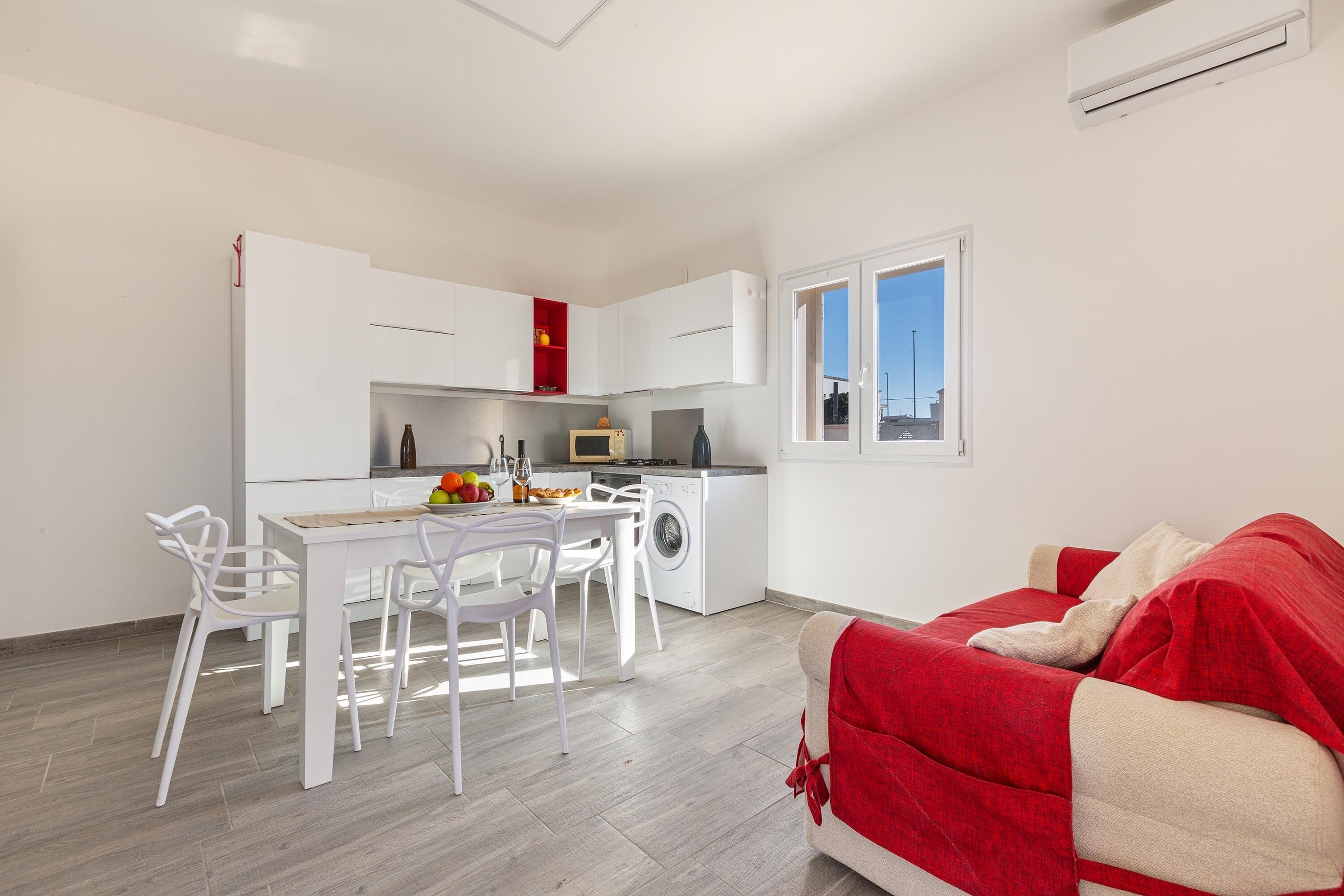 Un espacio habitable compacto con kitchenette, comedor y un sofá rojo.