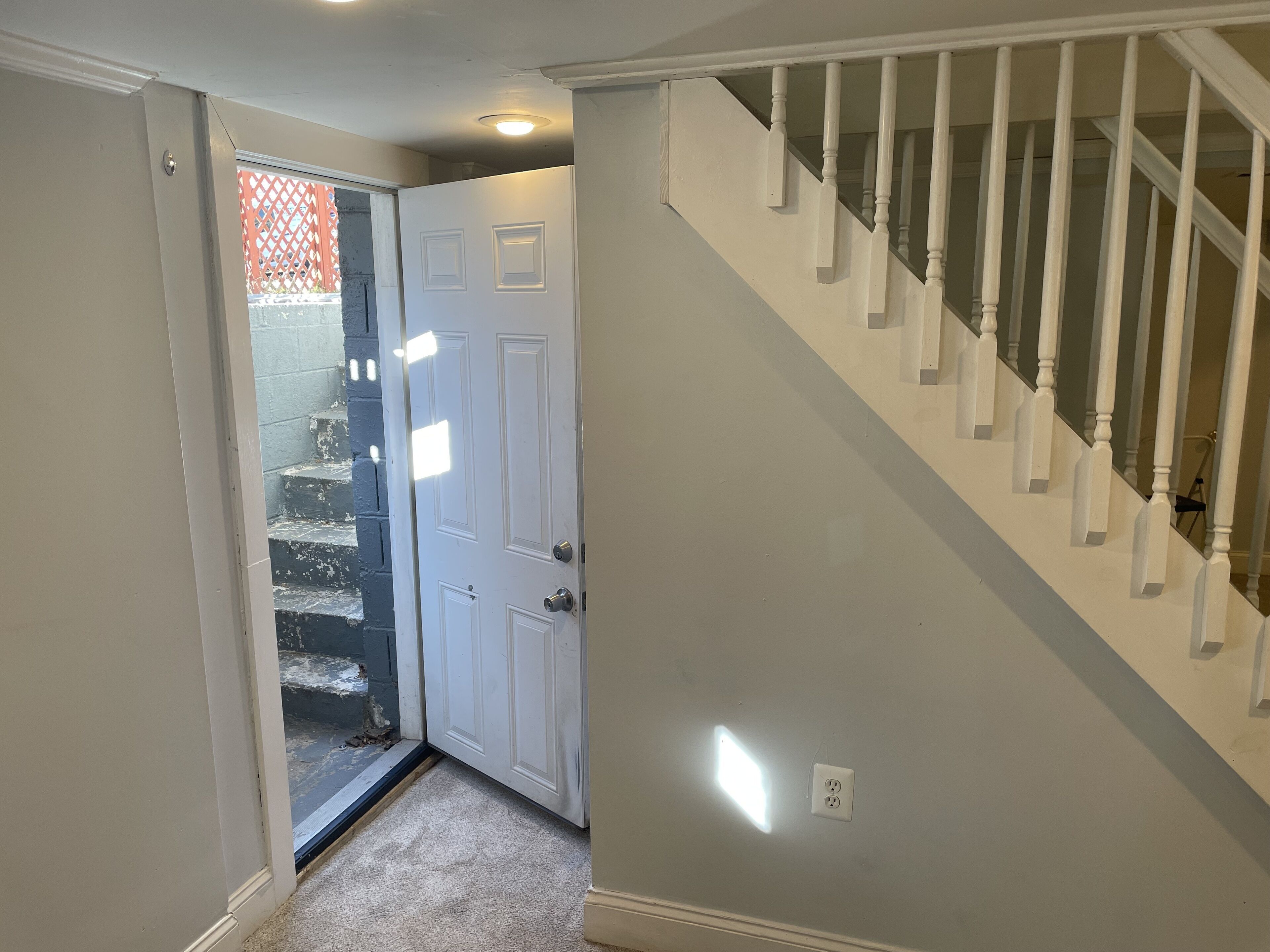 A hallway with a white door, a staircase with white balusters, and a light fixture on the wall.