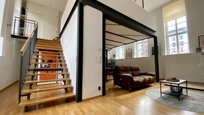 A spacious living area with a wooden staircase, a brown leather sofa, and a dining area. - Cityloft Gold - im Zentrum. Inkl. Parken, Netflix (Leipzig)